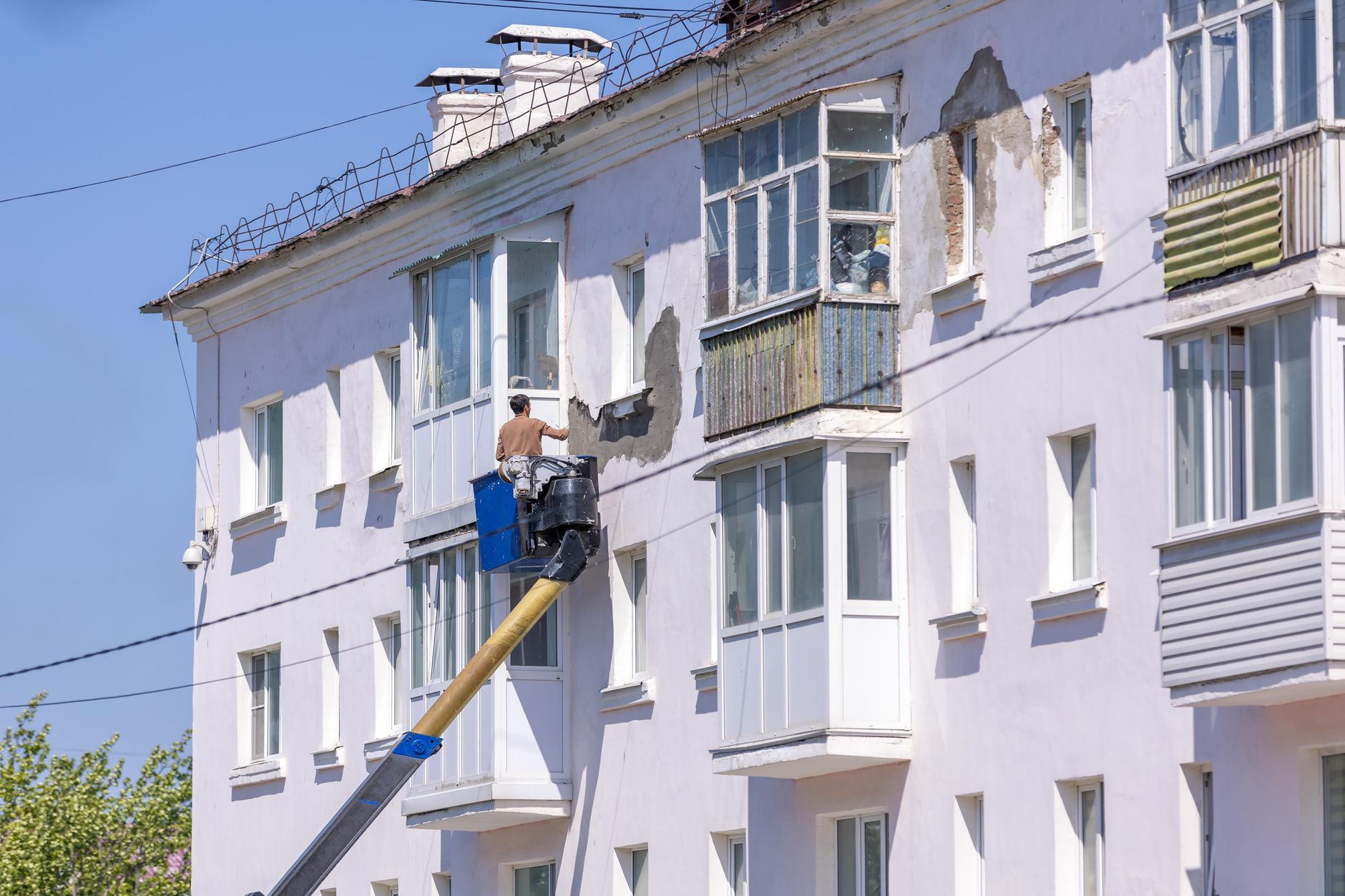 Worker renovating building facade using cherry picker on a sunny day.