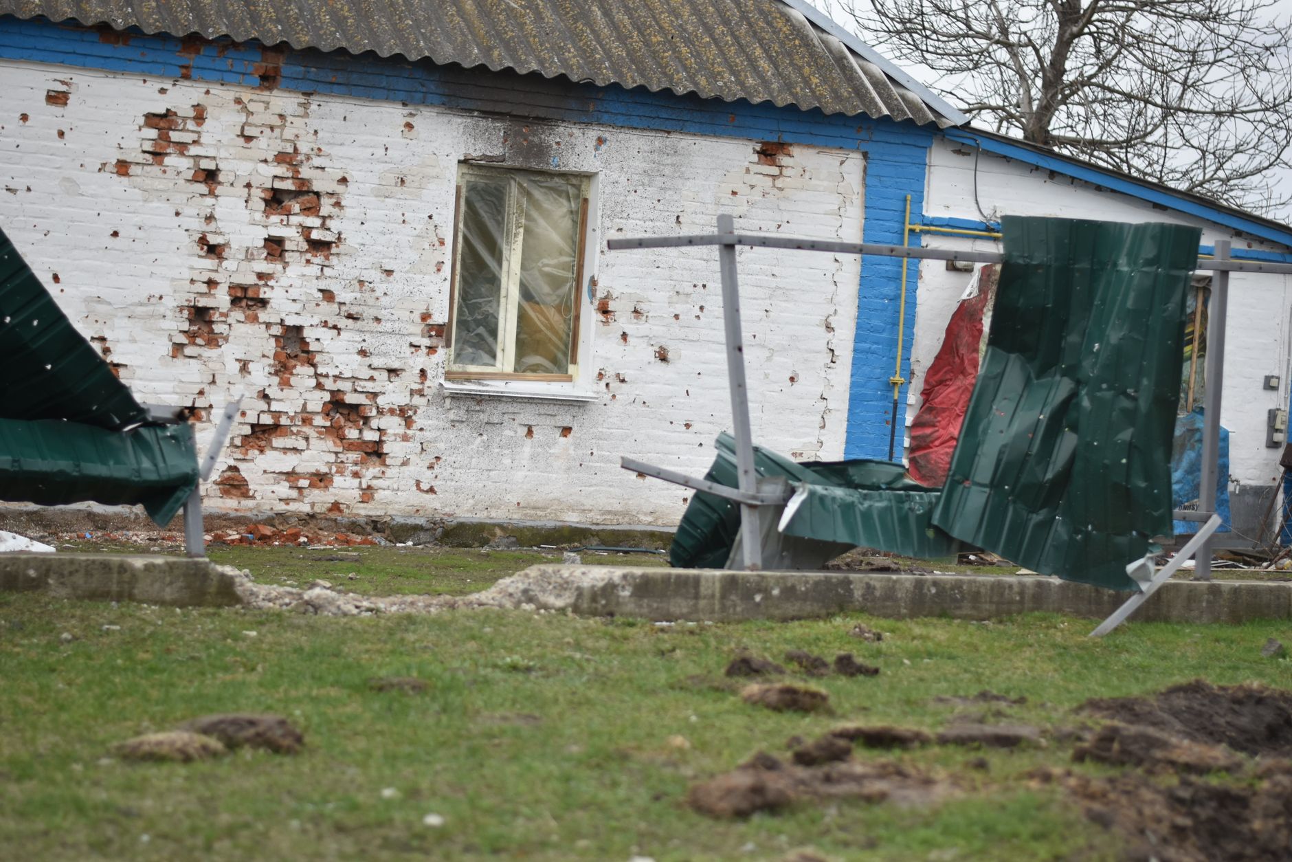 Rural house with damaged brick wall and broken fence, depicting decay and neglect.