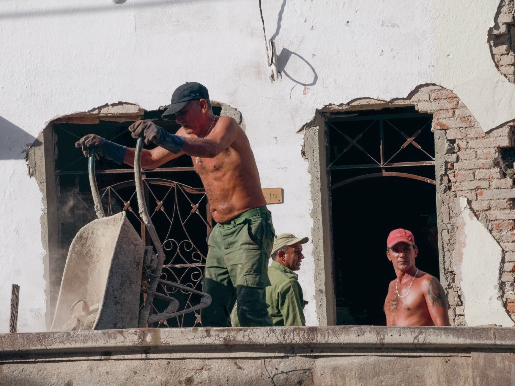 Three construction workers labor on a building renovation site on a sunny day.