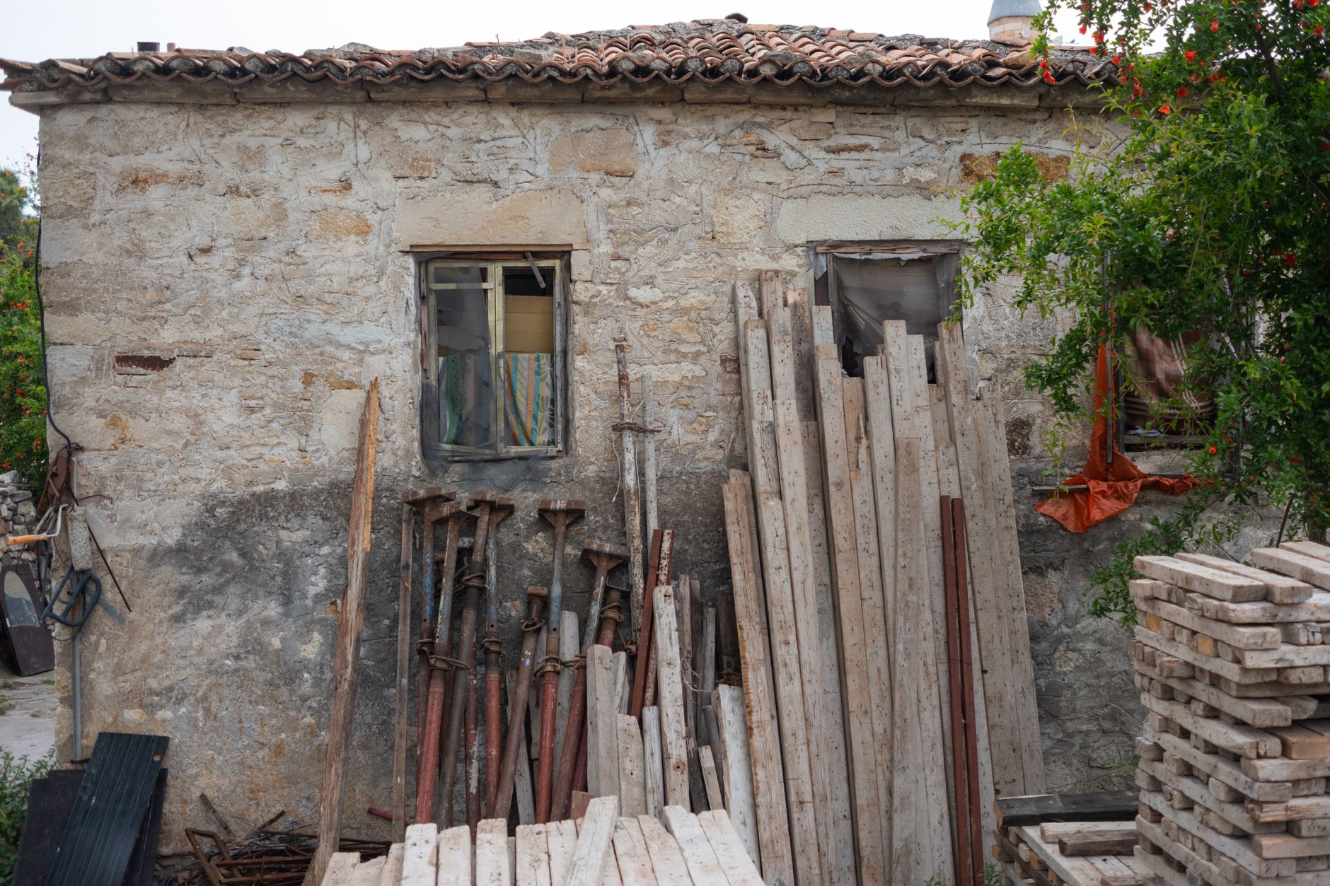 Rustic stone house in Foça, Turkey surrounded by construction materials and greenery.