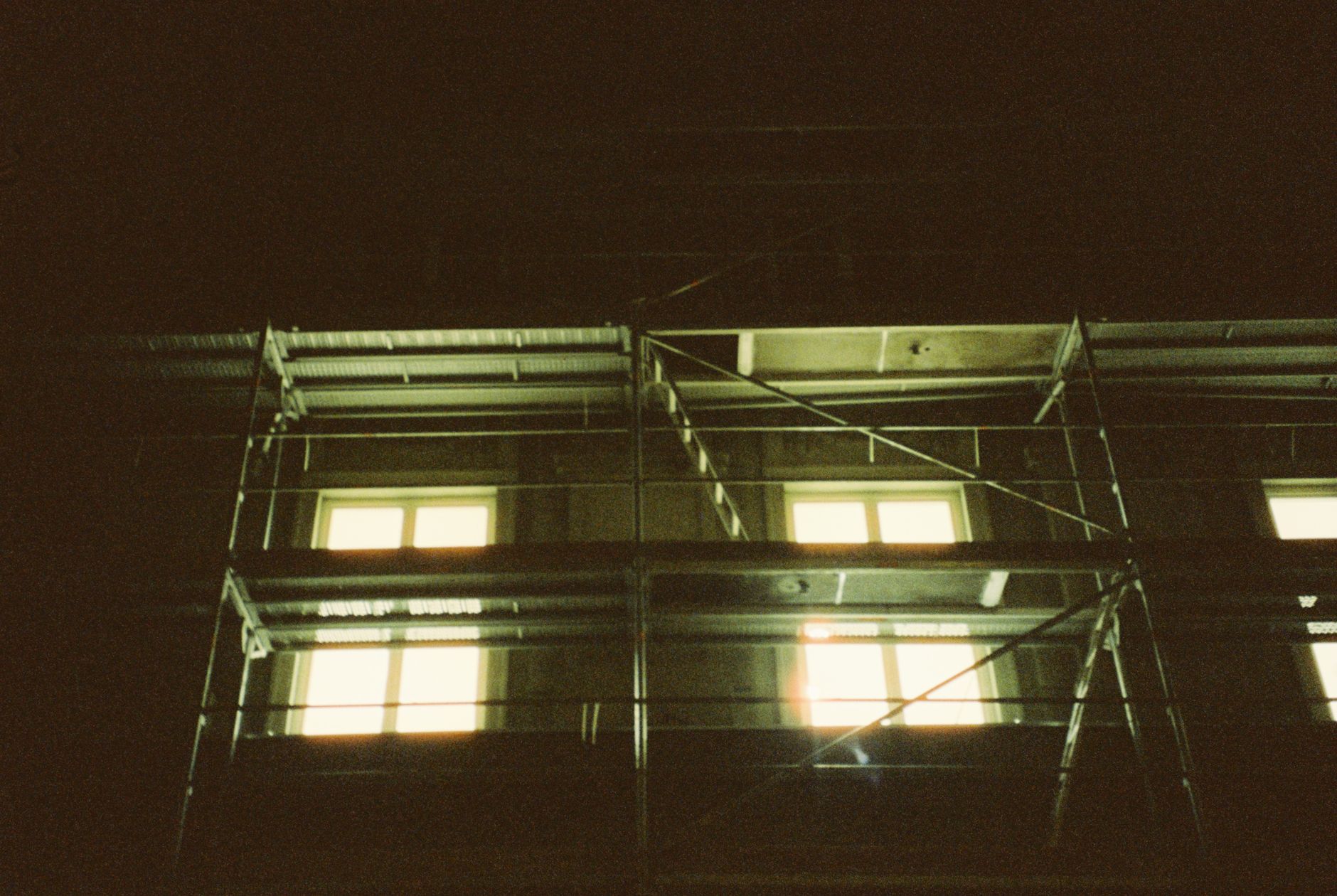 Photo of an apartment building with scaffolding and lit windows at night.