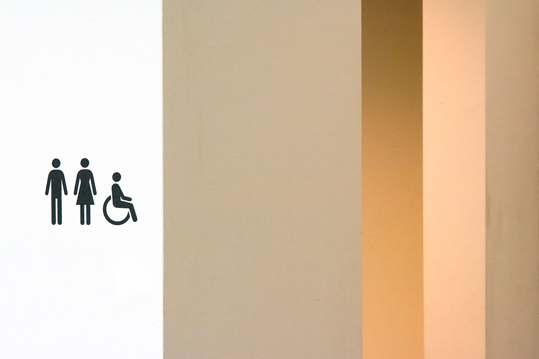Minimalist restroom sign featuring male, female, and wheelchair symbols on a modern wall.