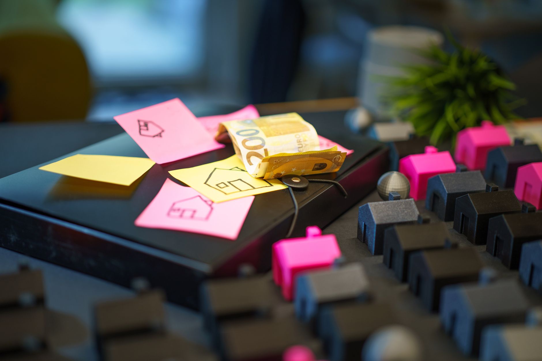 Euro banknotes on laptop with sticky notes and house models, symbolizing real estate investment.