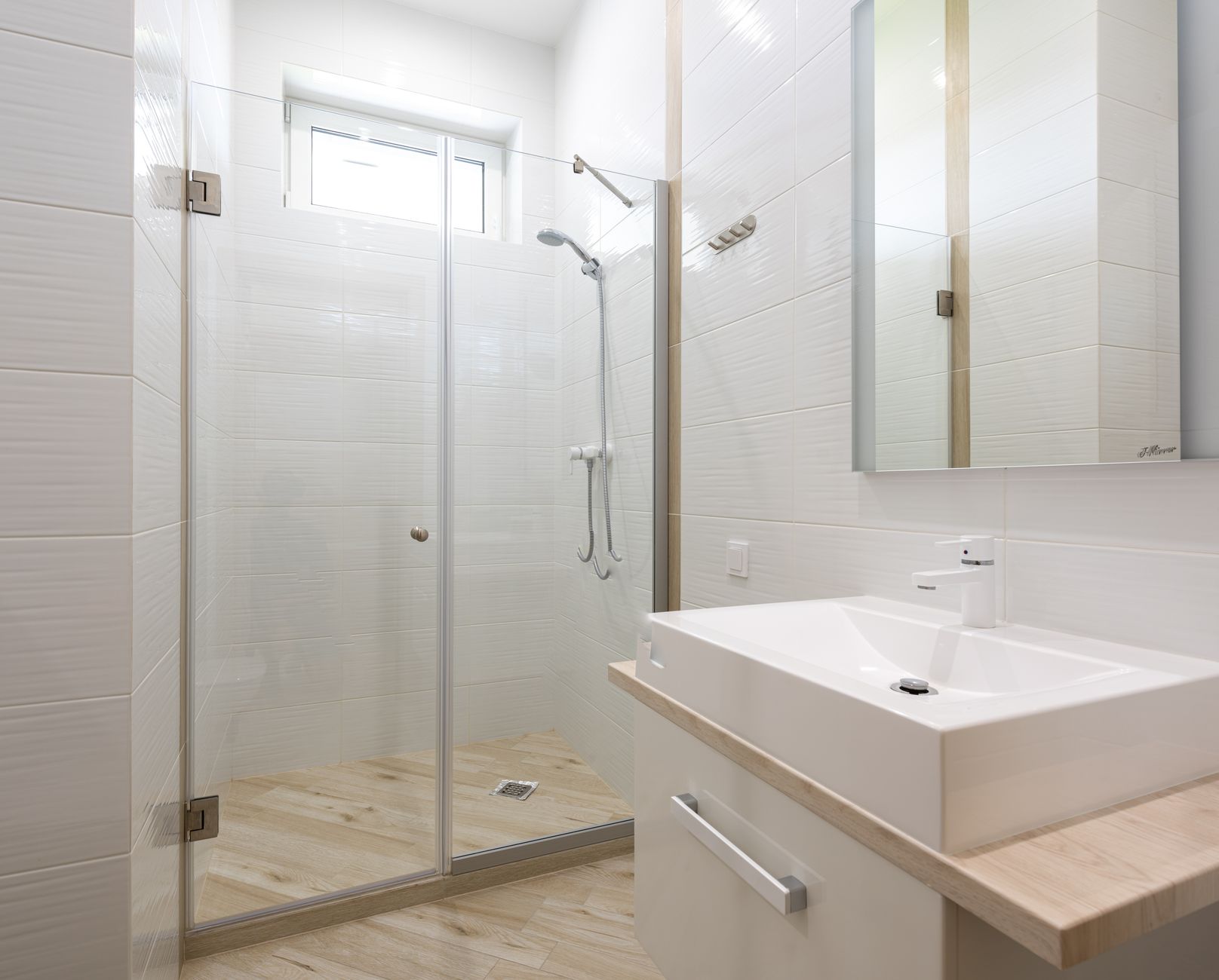 White sink at wall with cabinet and mirror placed near shower cabin with transparent glass door in modern stylish light bathroom