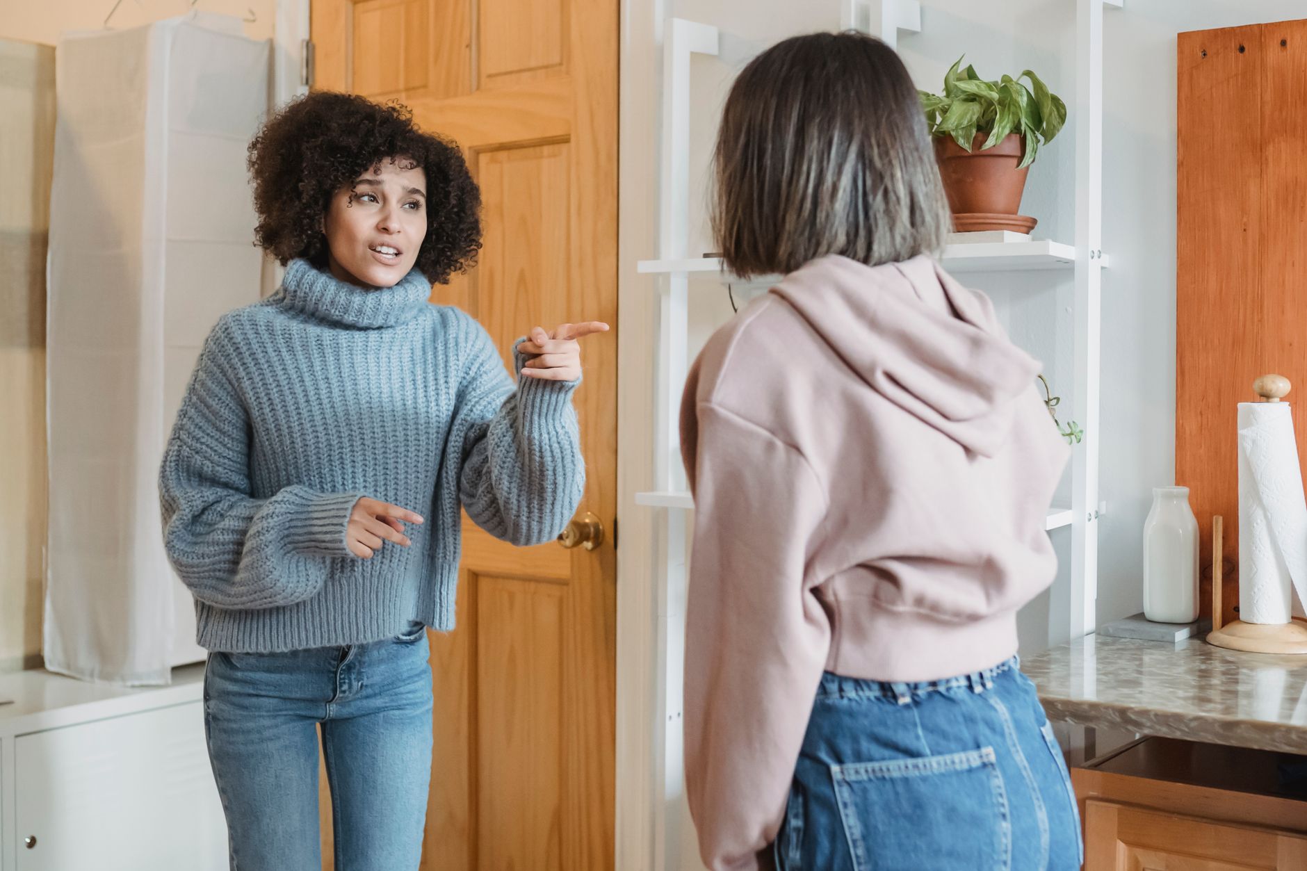 Angry African American female complaining and pointing at faceless female while having fight i modern flat with green plants