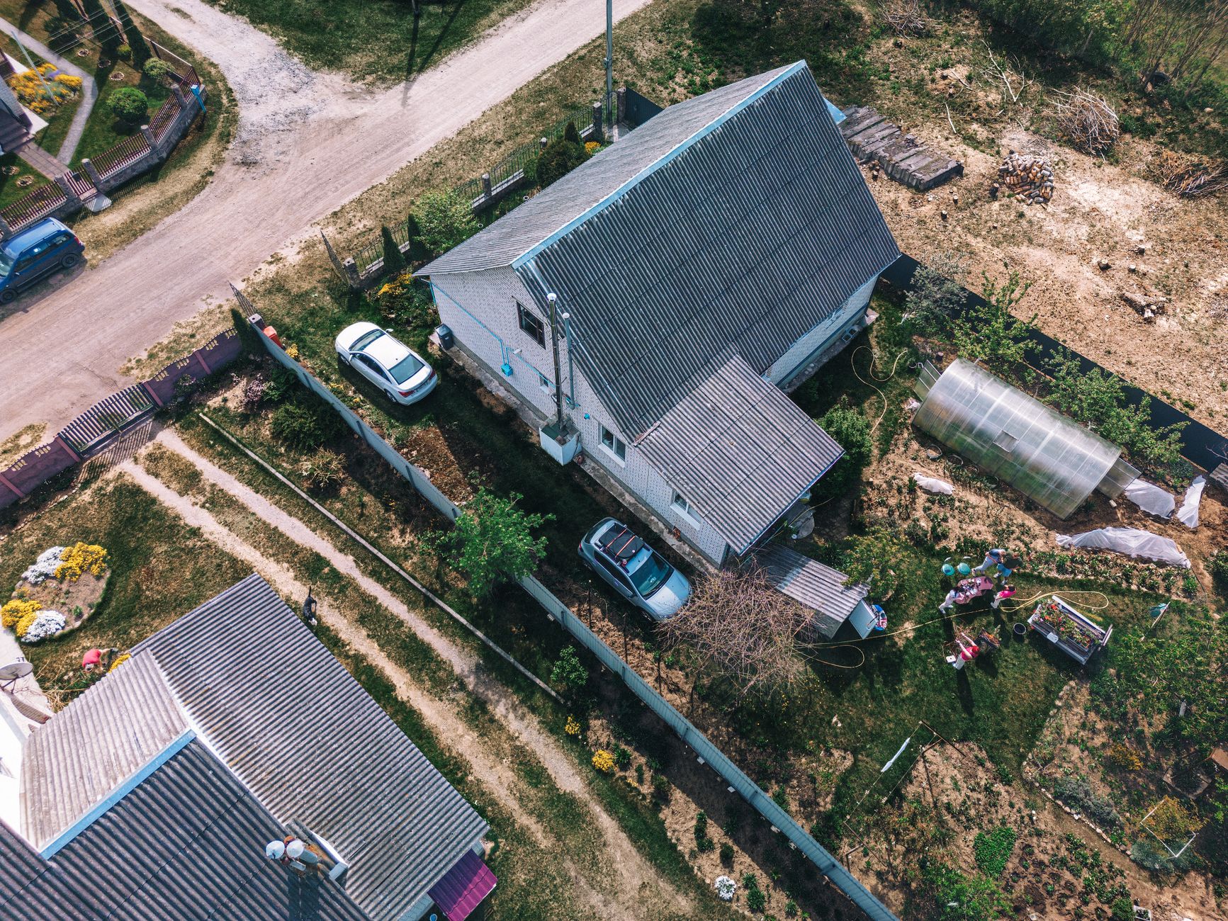 Aerial photo of a rural house with garden, greenhouse, and parked cars in Belarus. Shot in clear daylight.
