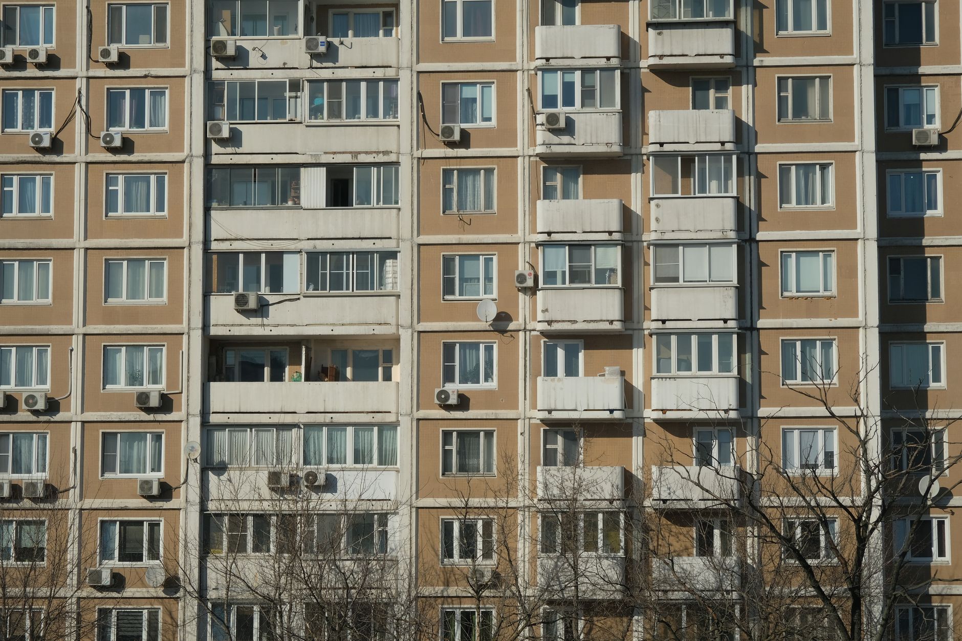 Front view of a sunlit urban apartment building with balconies and air conditioning units.