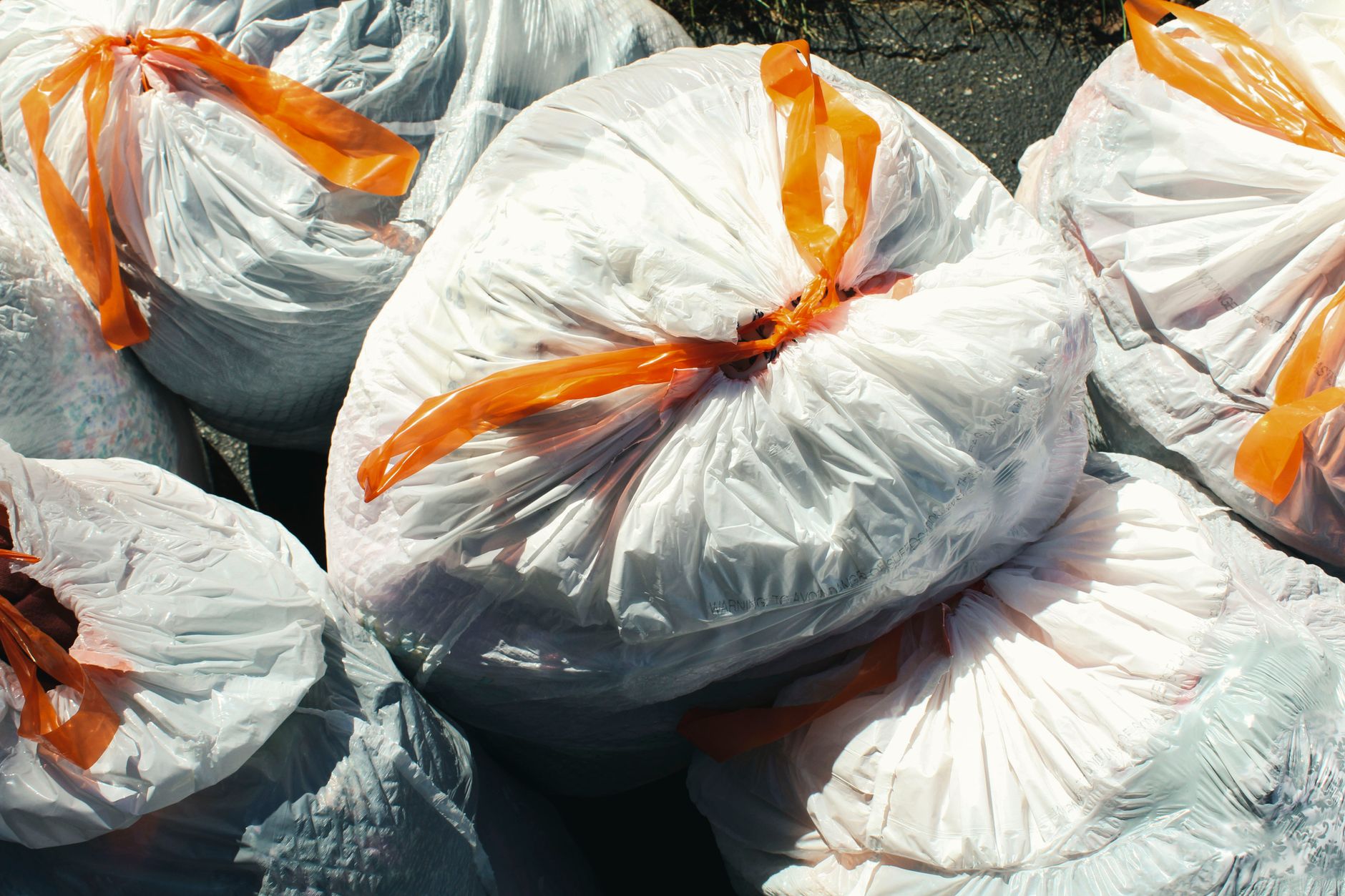 Bags of waste sealed with orange ties viewed from above.