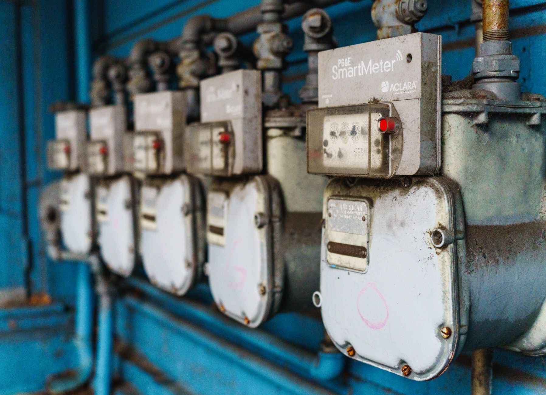 Multiple smart utility meters lined up on a blue industrial wall.