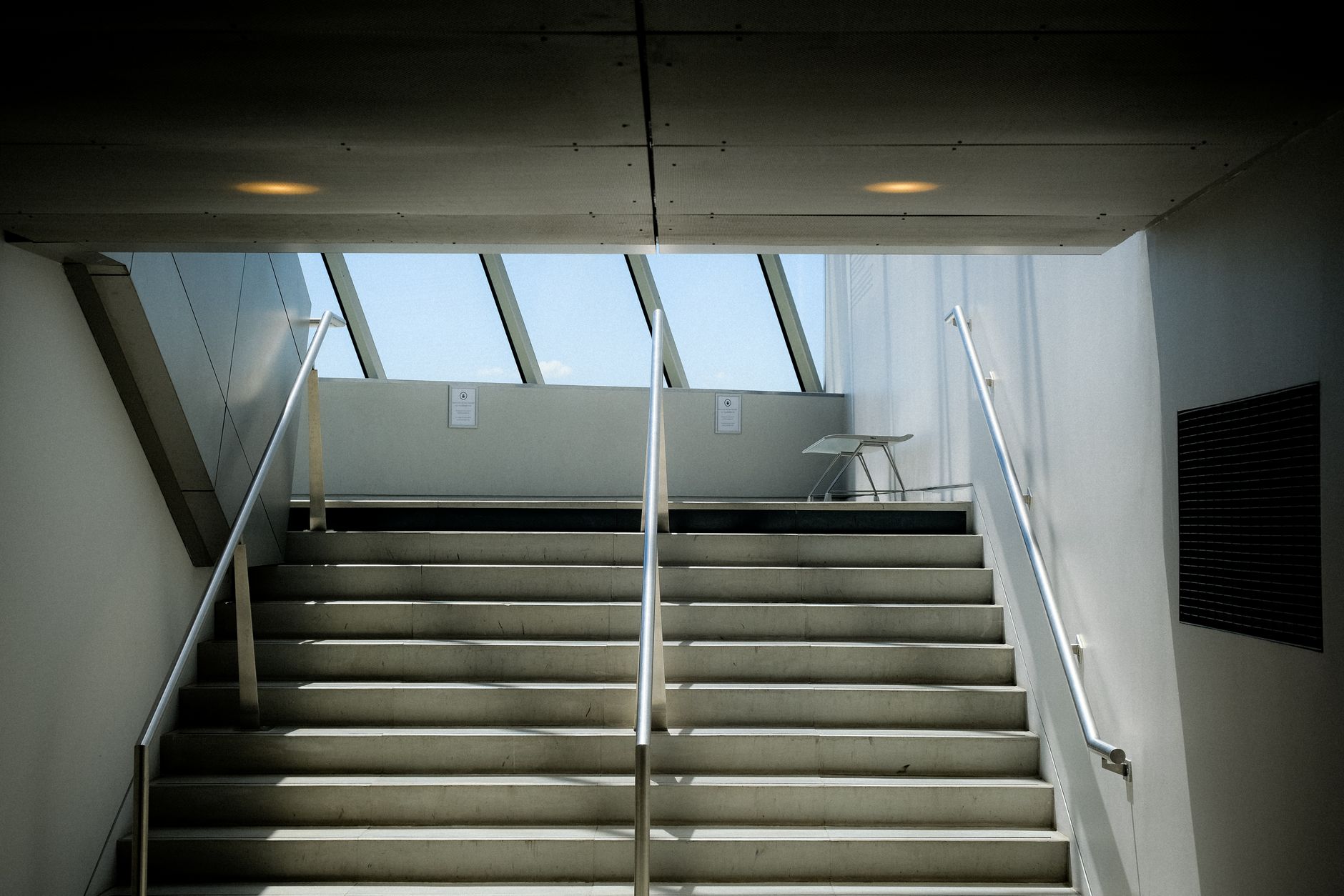 A contemporary indoor staircase featuring concrete steps and metal railings with natural light from skylights.