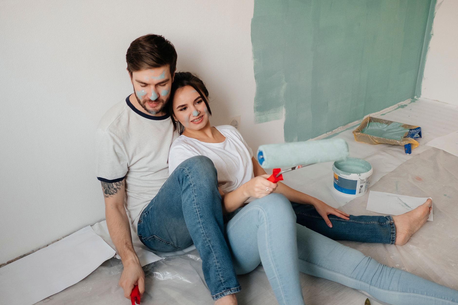 Young couple enjoying a playful and creative home renovation with paint rollers indoors.