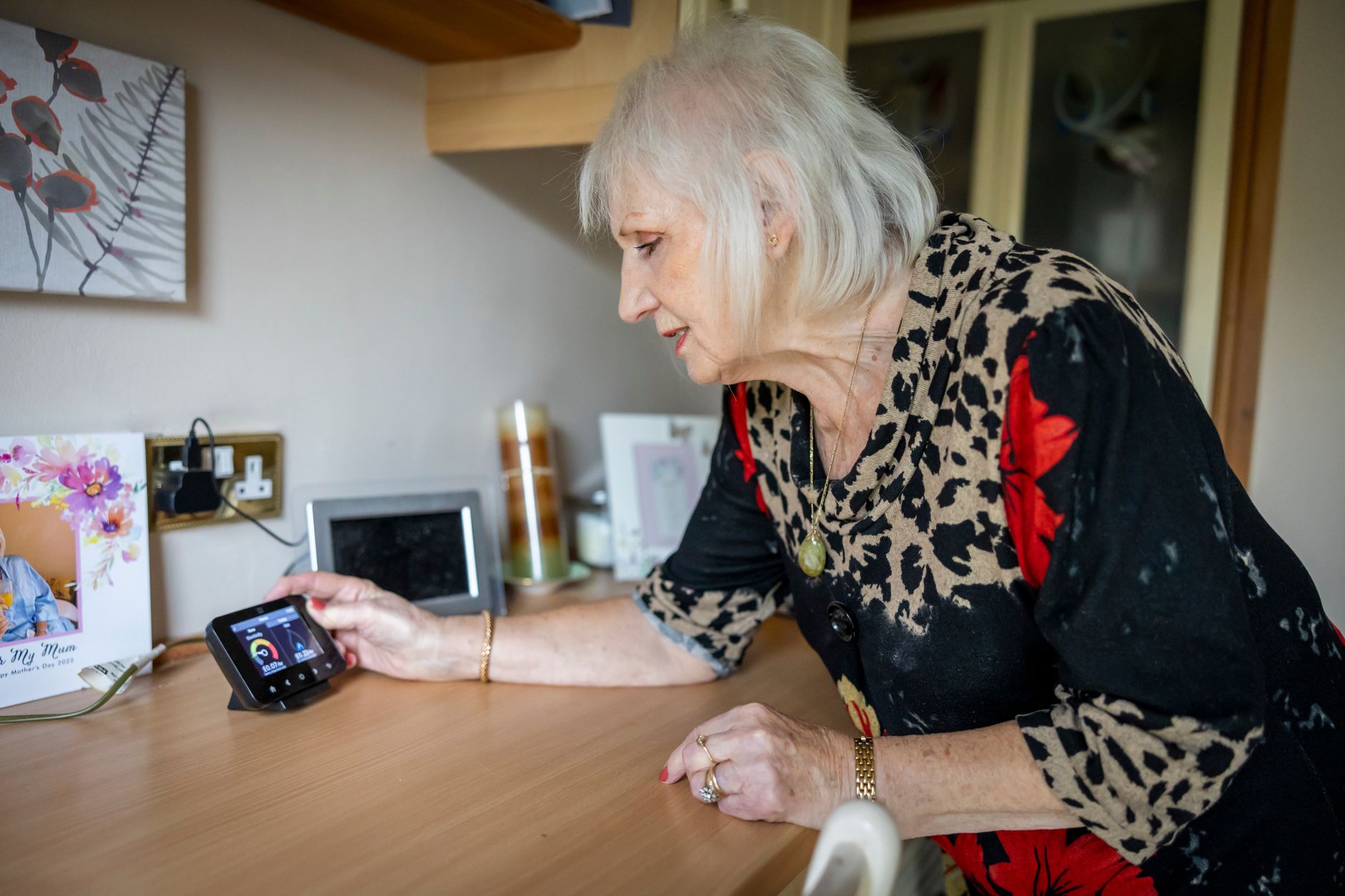 An elderly woman interacts with a smart meter on a desk, illustrating energy management in modern technology.