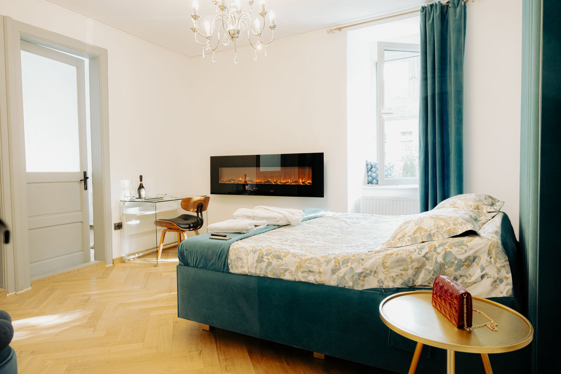 Chic bedroom featuring a modern electric fireplace, elegant chandelier, and parquet flooring.