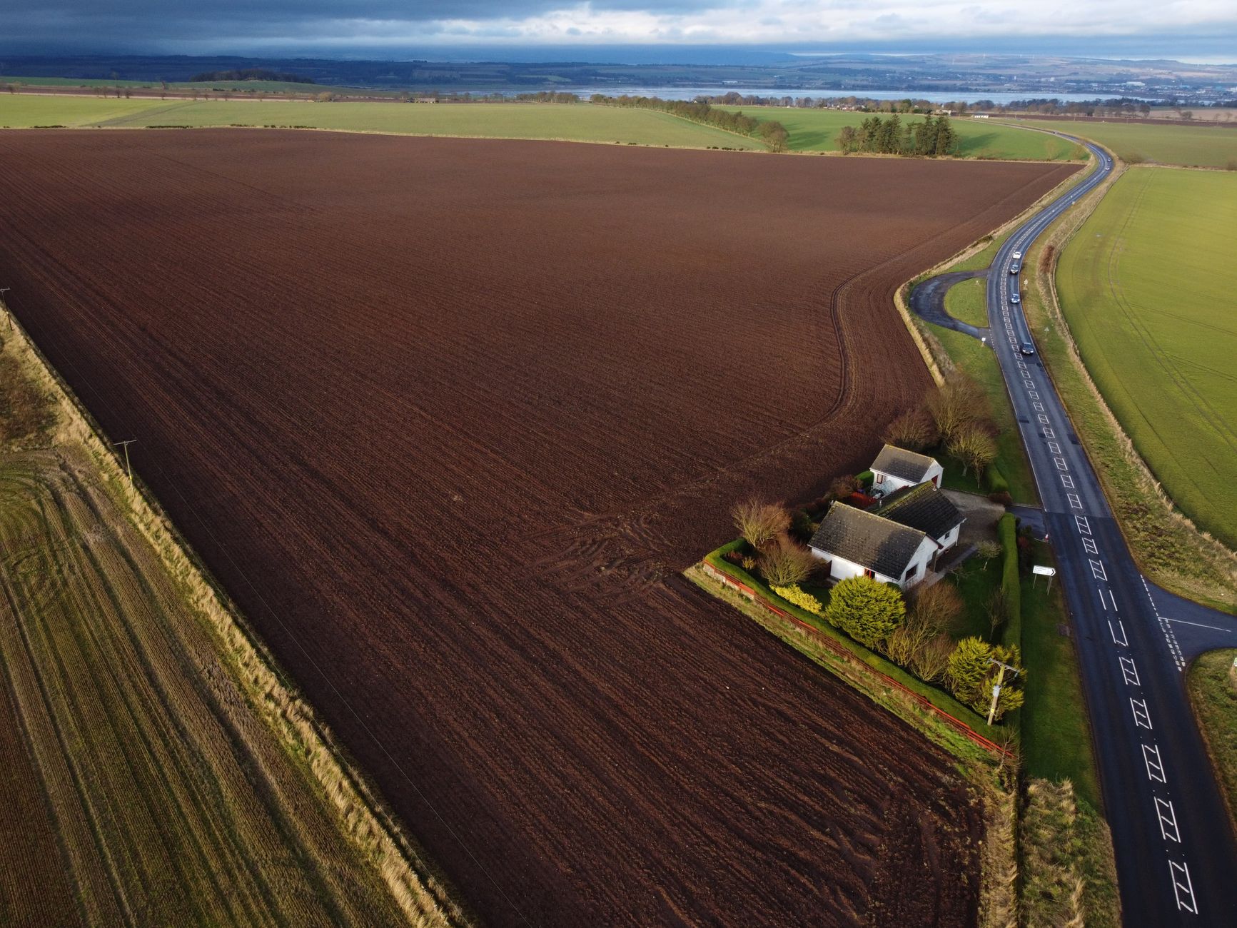 Aerial shot of expansive farmland with a cottage and road in rural Scotland.