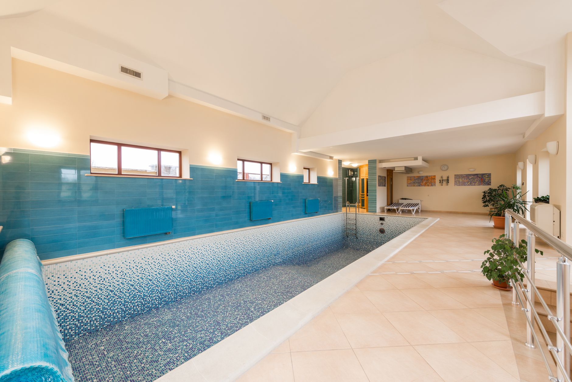 Empty spacious pool in building with tile floor near potted green plants and windows