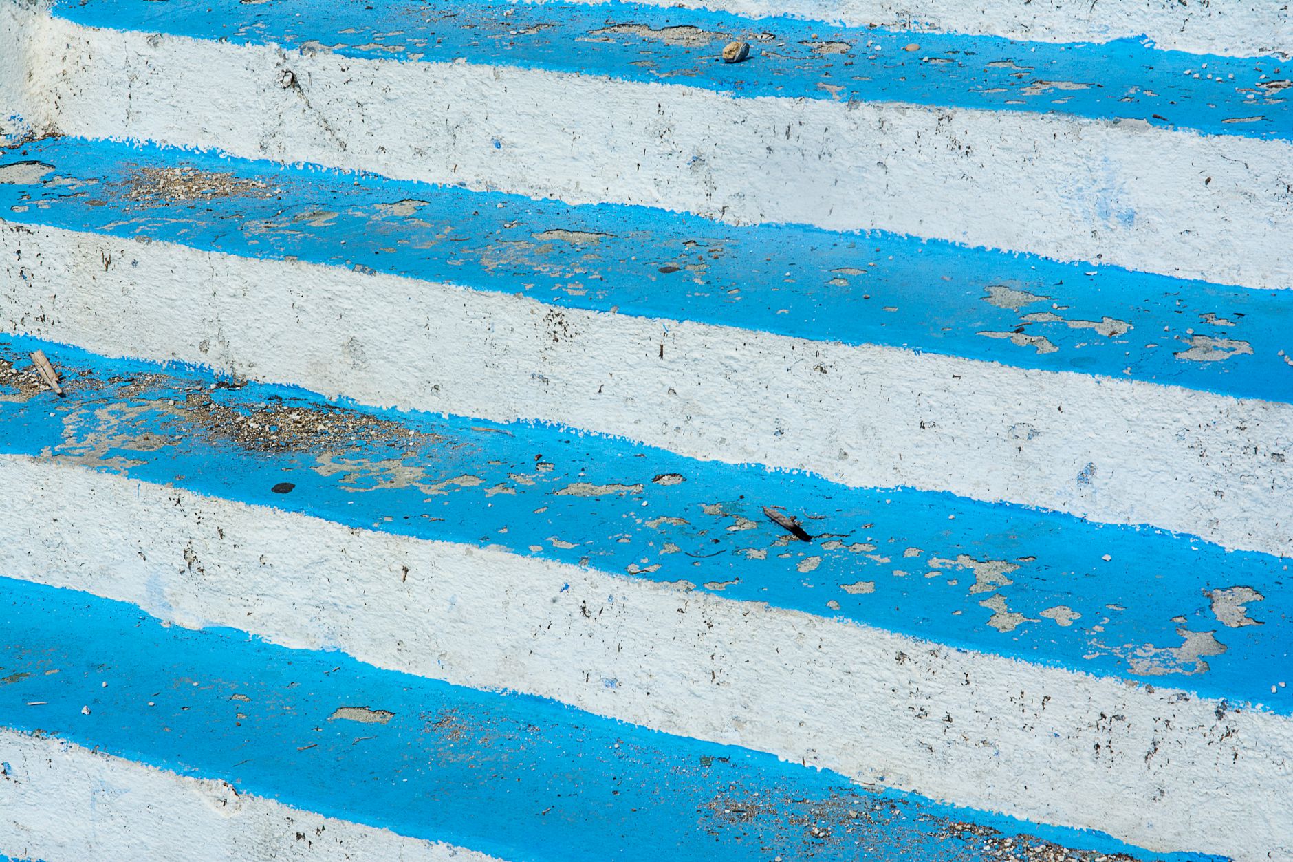 Close-up of worn blue and white striped concrete steps, showing texture and decay.
