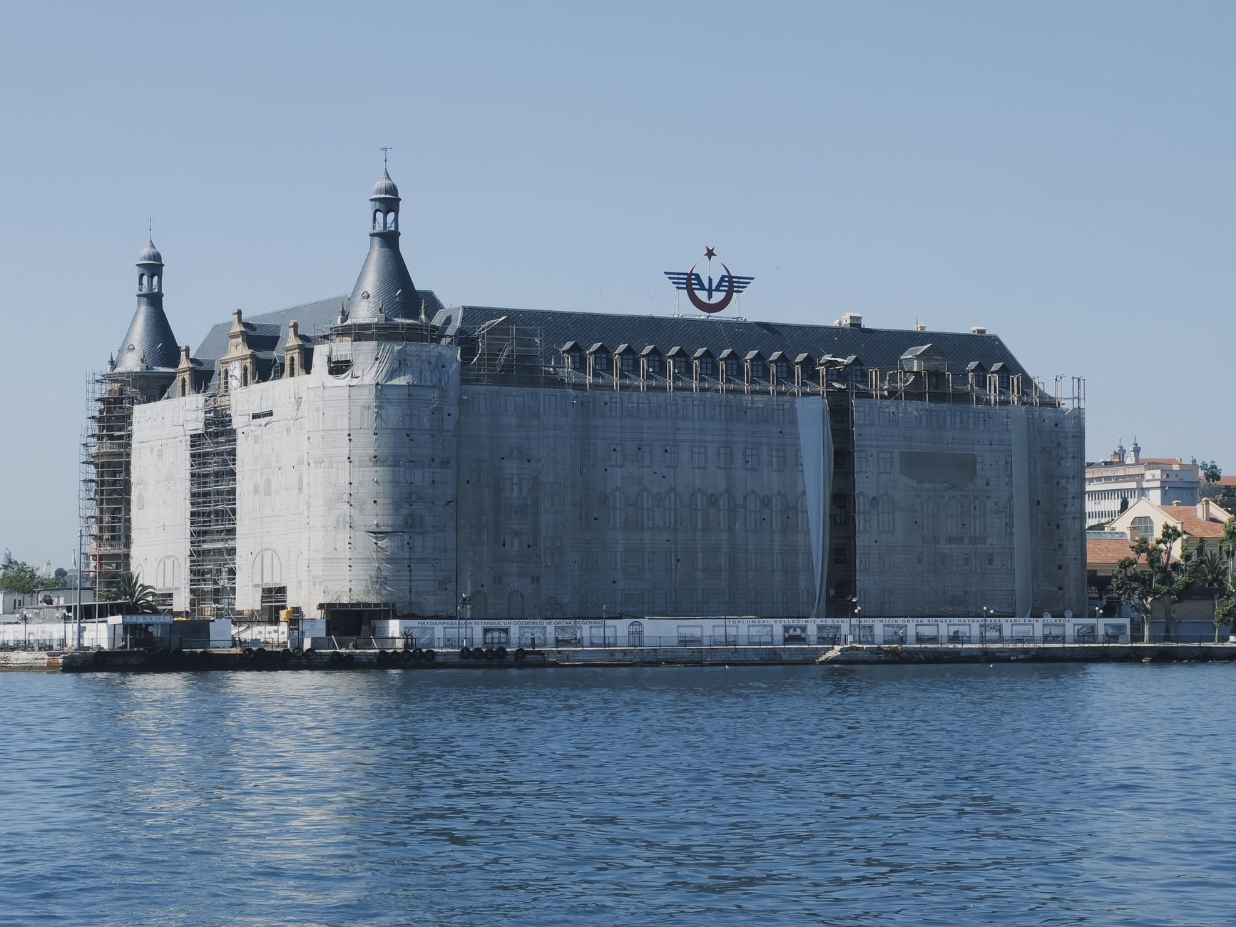 View of a historic building under renovation covered with scaffolding by a river.