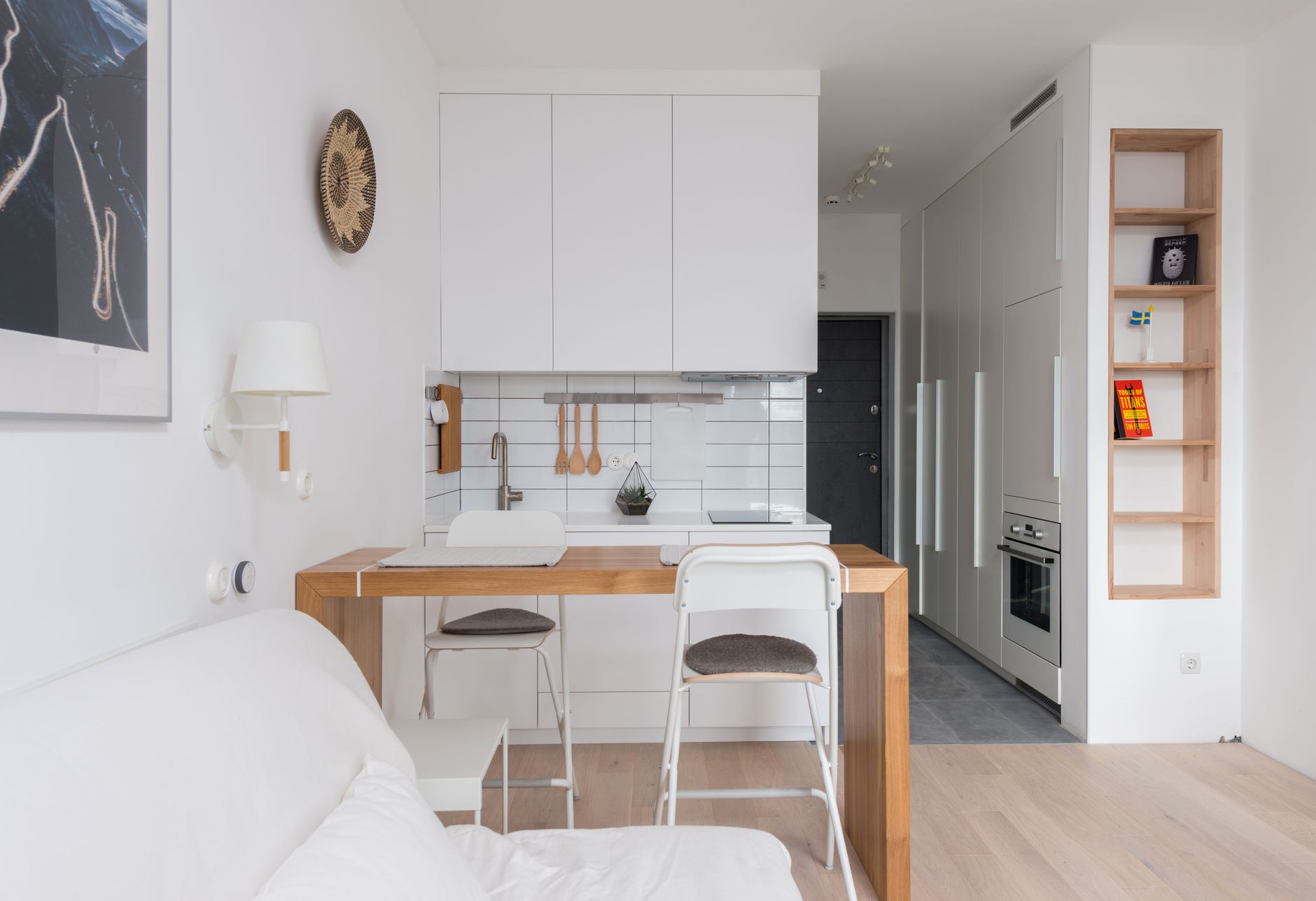Wooden counter with chairs separating kitchen zone from living room in modern light apartment