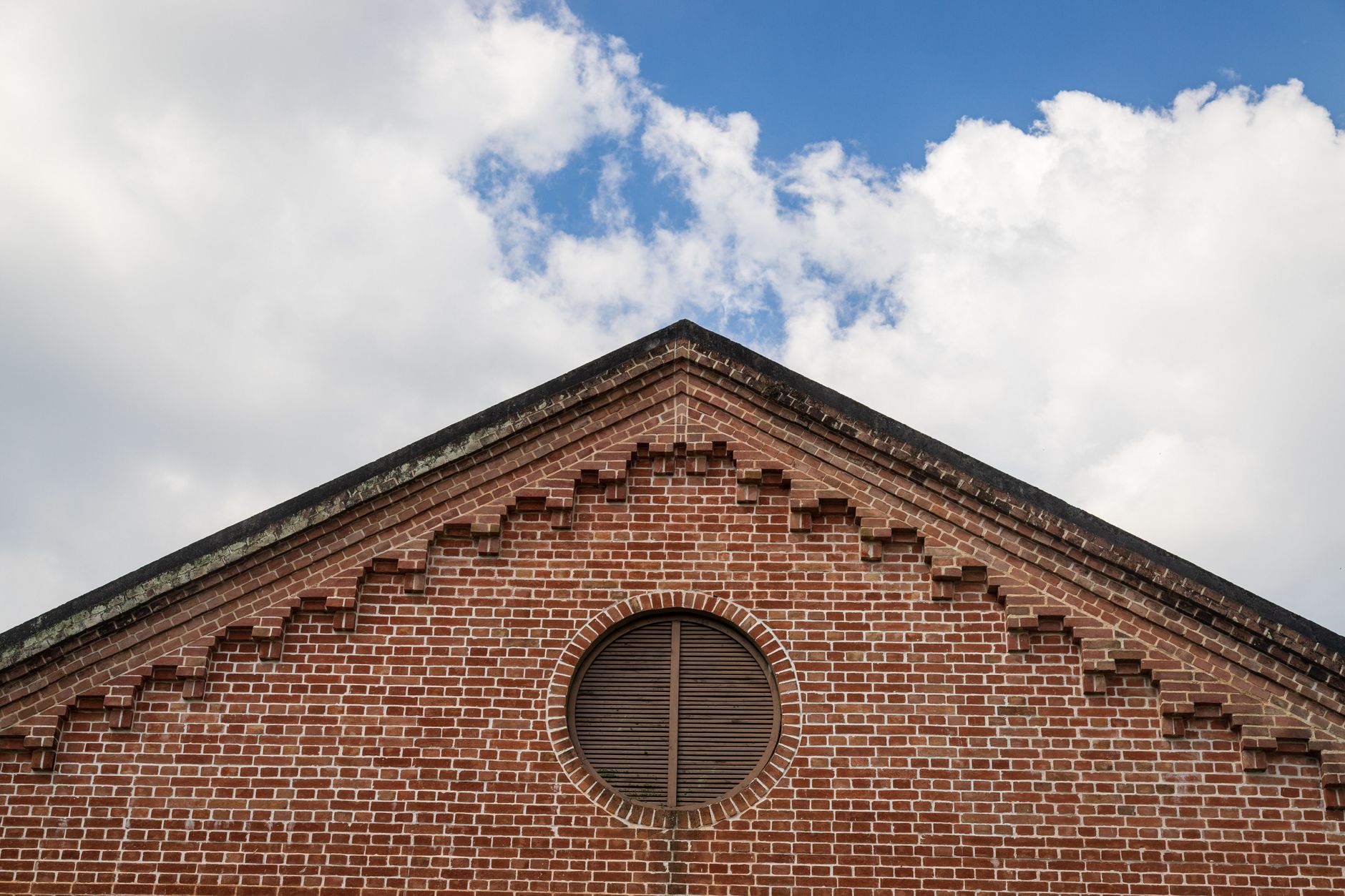 Architectural detail of a brick gable against a bright blue sky with clouds.