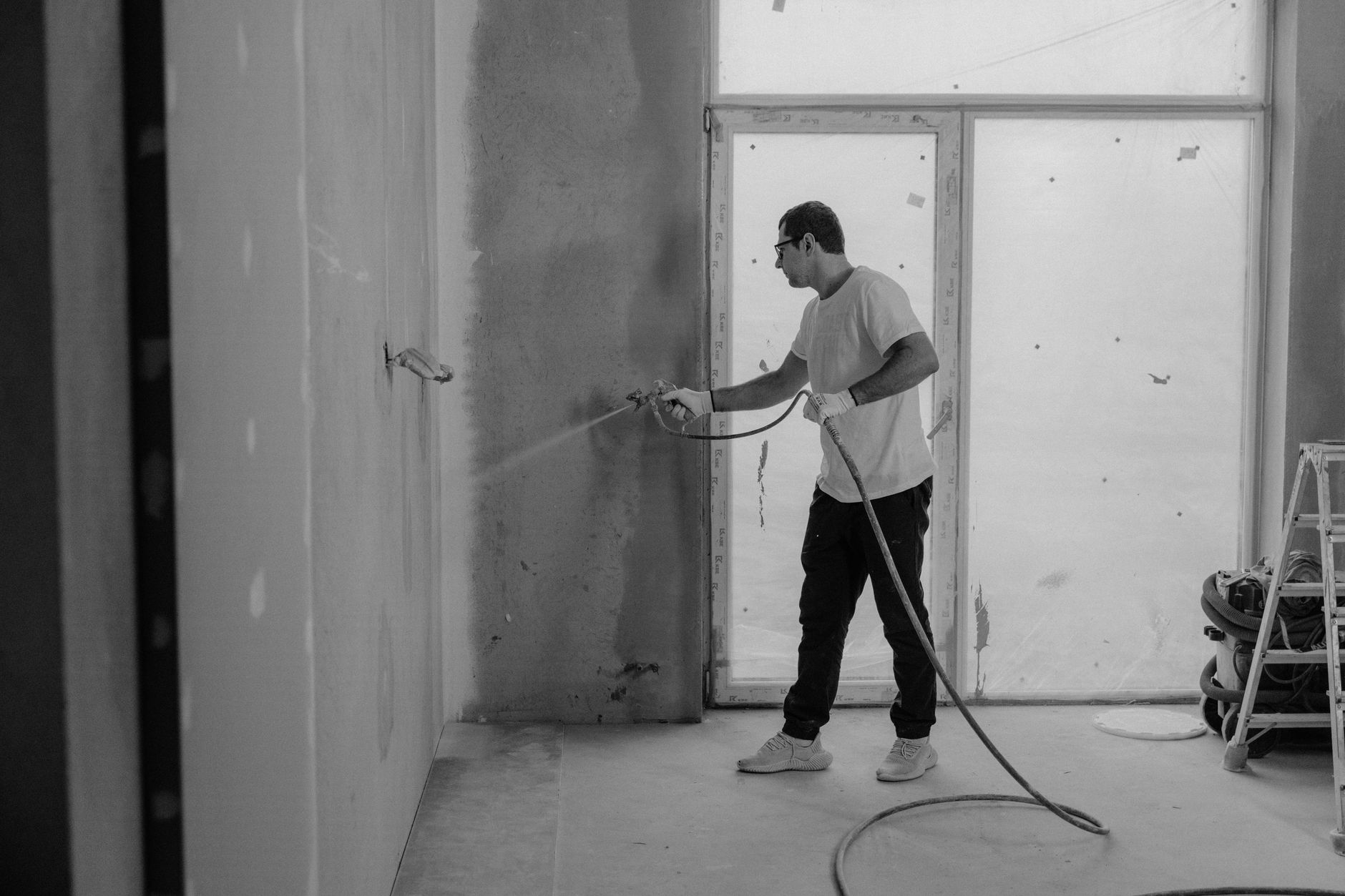 A worker paints an interior wall with a spray gun during a renovation project.