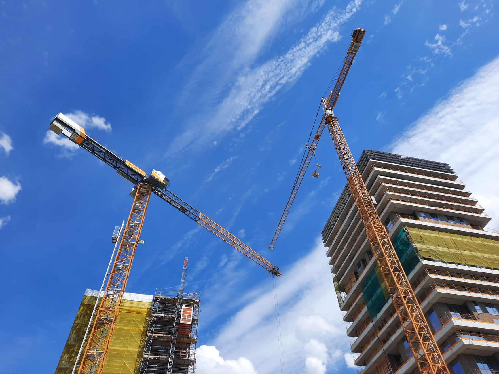 Low angle view of tower cranes and building under construction against a blue sky.