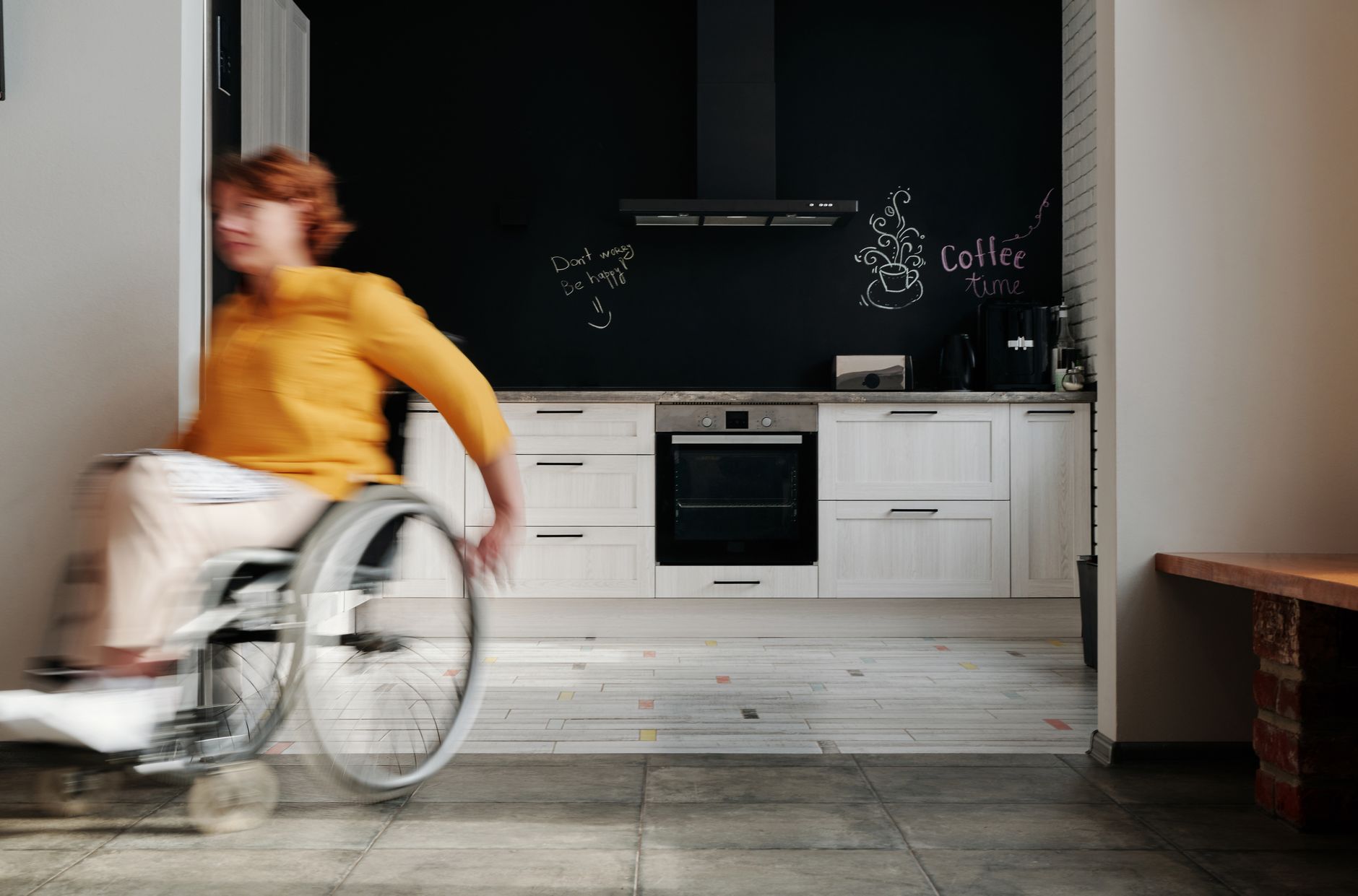 A woman in a wheelchair moving through a modern kitchen with chalkboard wall art.