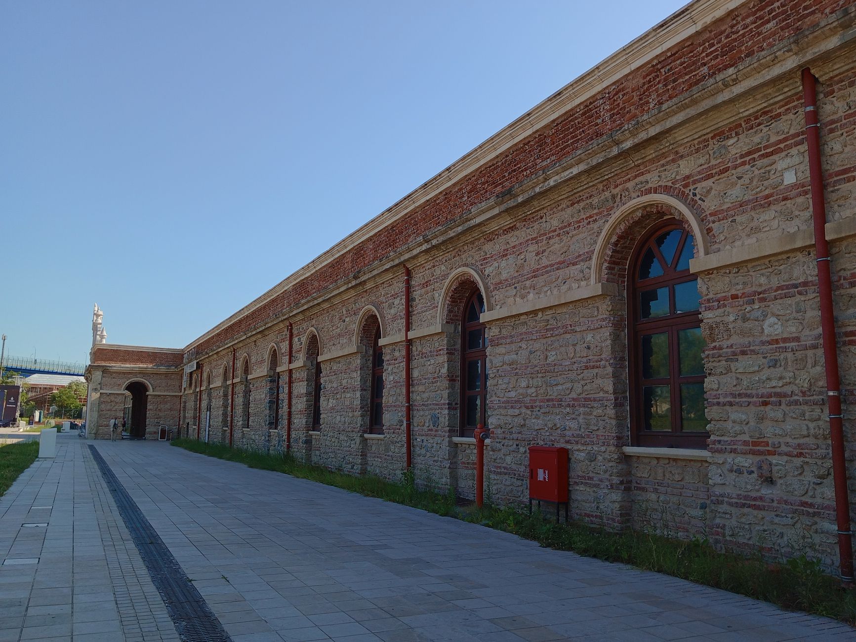 A long historic brick building featuring arched windows and a serene walkway.