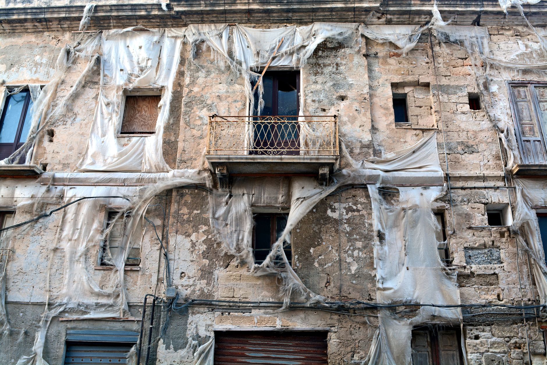An abandoned and weathered building facade in Sicily, Italy with ripped sheets covering the structure.