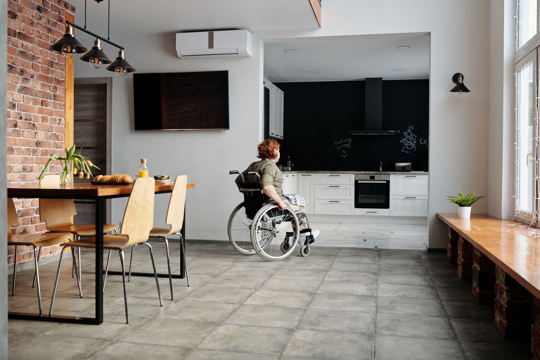 A woman in a wheelchair in a modern kitchen and dining space, highlighting accessibility.