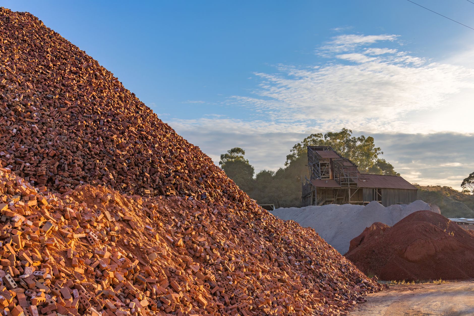 Large piles of red bricks and sand in a construction site with rustic buildings.