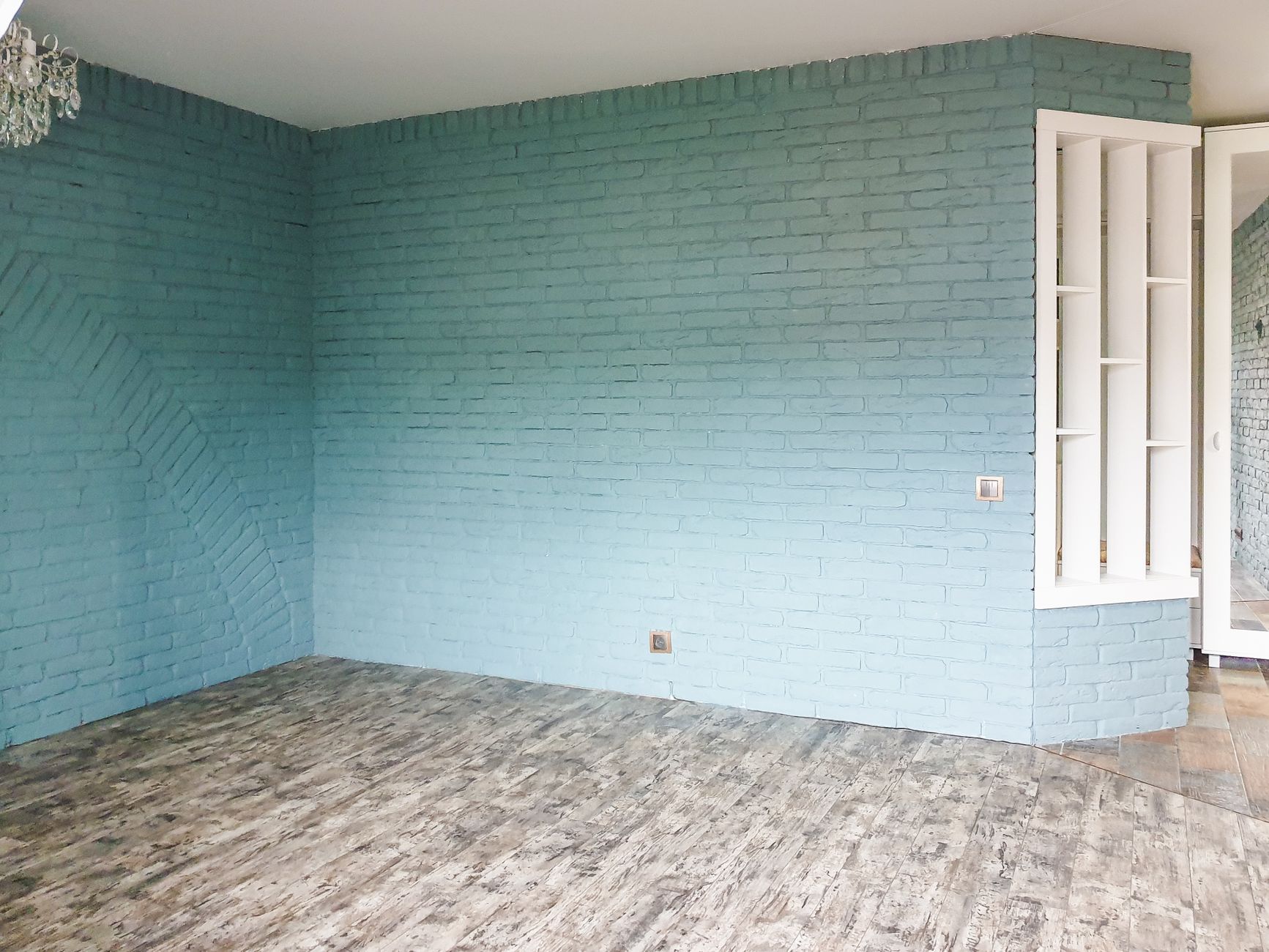 Spacious empty room featuring a stylish blue brick wall and rustic wooden flooring.