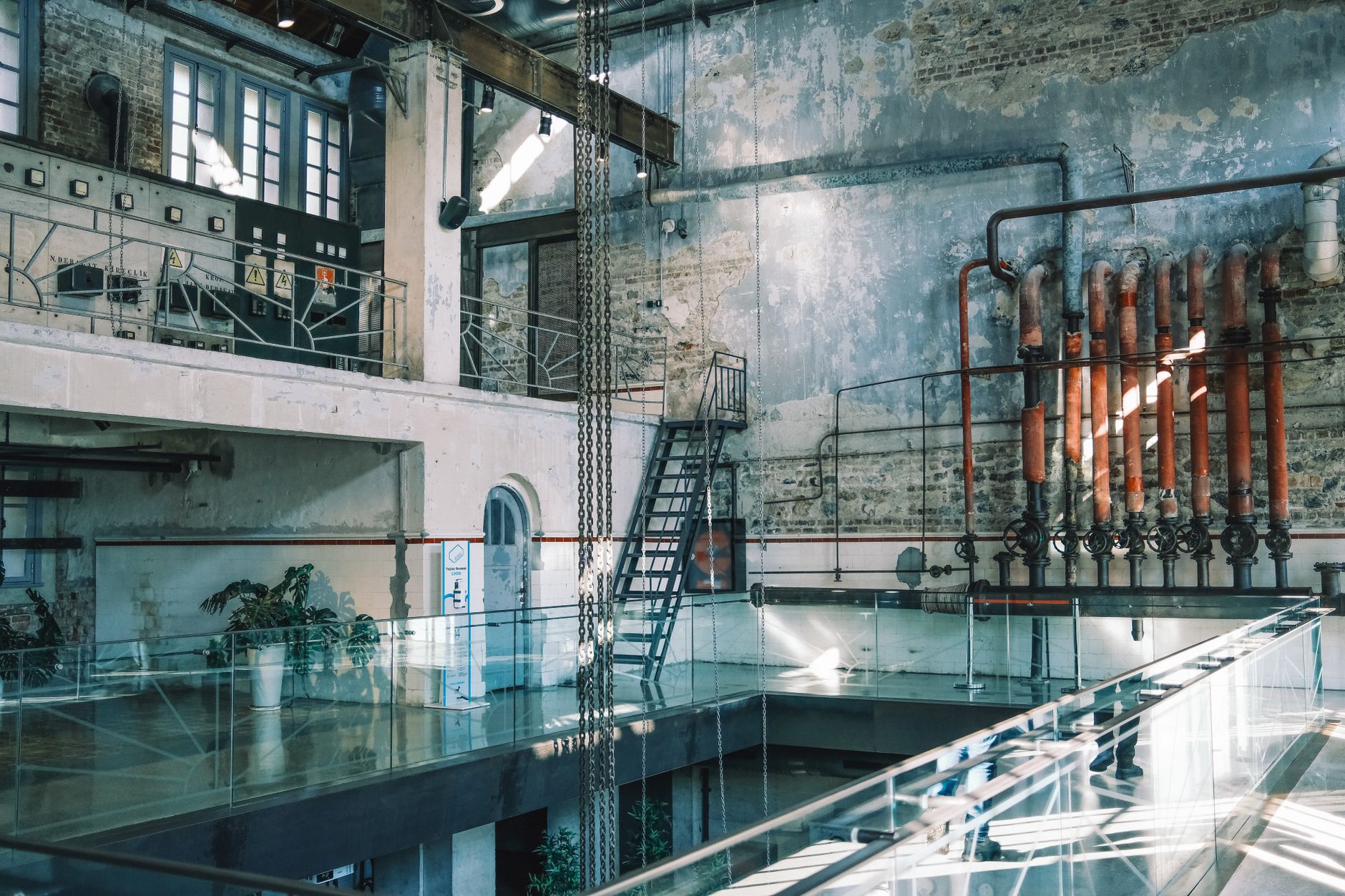 A vintage industrial interior with exposed pipes, brick walls, and metal staircases, captured in natural light.
